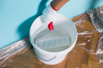 Image of paint can and man holding paint roller in front of blue wall.