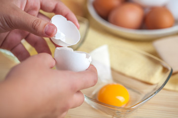 Woman hands breaking an egg to separate egg white and yolks, egg shells at the background