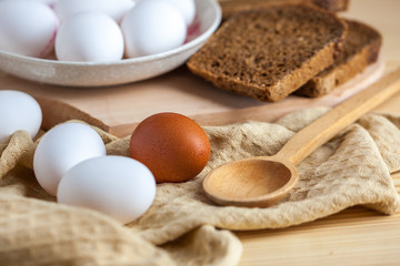 white and brown eggs with bread on a wooden table, a towel and a wooden spoon