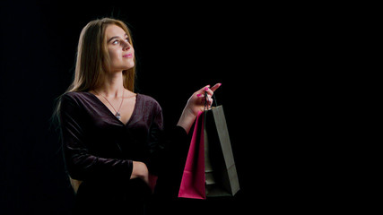 Sale. Young smiling woman showing shopping bag in black friday holiday. Girl on dark background with copy space