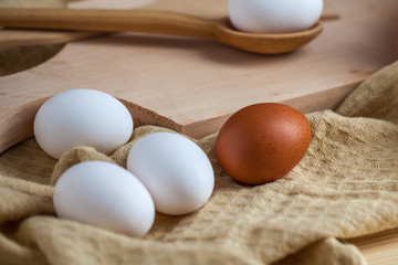 white and brown eggs on a wooden table, a towel and a wooden spoon