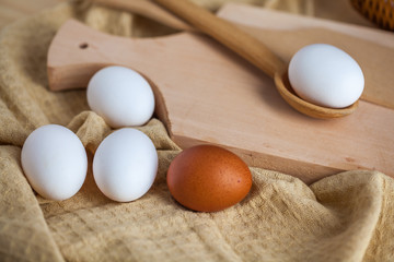 white and brown eggs on a wooden table, a towel and a wooden spoon