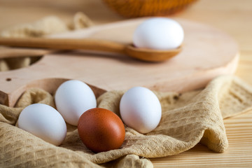 white and brown eggs on a wooden table, a towel and a wooden spoon