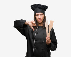 Young hispanic cook woman wearing chef uniform with angry face, negative sign showing dislike with thumbs down, rejection concept