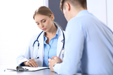 Fototapeta premium Doctor and patient in hospital. Beautiful blonde physician consulting business man about his health. Medicine concept