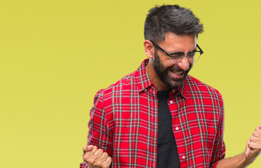 Adult hispanic man wearing glasses over isolated background very happy and excited doing winner gesture with arms raised, smiling and screaming for success. Celebration concept.