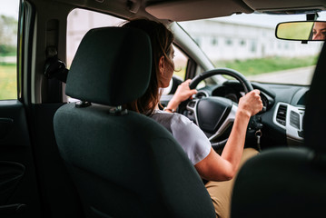 Lifestyle shot of young cheerful woman driving car, rear view.