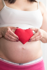 Pregnant woman holding a red heart on her belly