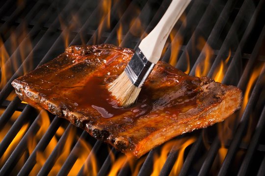 Spare ribs being brushed with marinade on a hot grill
