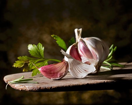 A garlic bulb and flat-leaf parsley on a wooden board