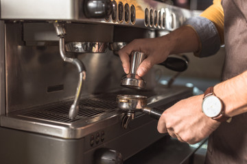cropped shot of barista pressing coffee into holder for coffee machine