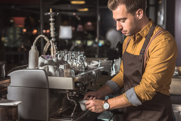 Fototapeta na wymiar handsome young barista preparing coffee with coffee machine in cafe