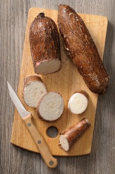 Cassava root, partially sliced, on a chopping board with a knife