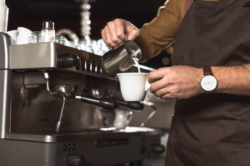 cropped shot of barista pouring milk into coffee while preparing it in cafe