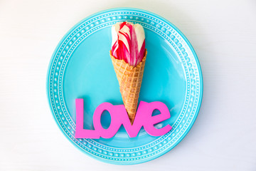 Tulip  flower in the ice cream waffle cone on plate with Love word