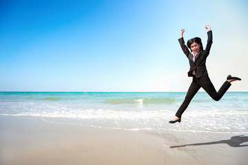 Obraz premium Business competition: businesswoman jumping with hand on the beach, meaning of winner