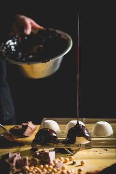 A confectioner glazing pralines with melted chocolate