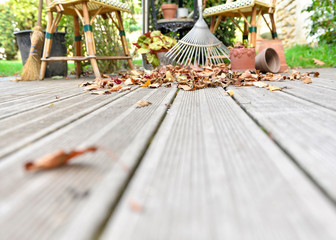 rake on dry  leaves on the floor of a wooden terrace in autumn