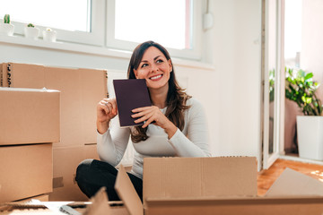 Portrait of a happy woman sitting on the floor among boxes with a book. Moving to a new apartment.