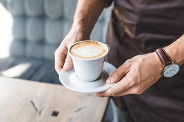cropped shot of waiter holding cup of cappuccino
