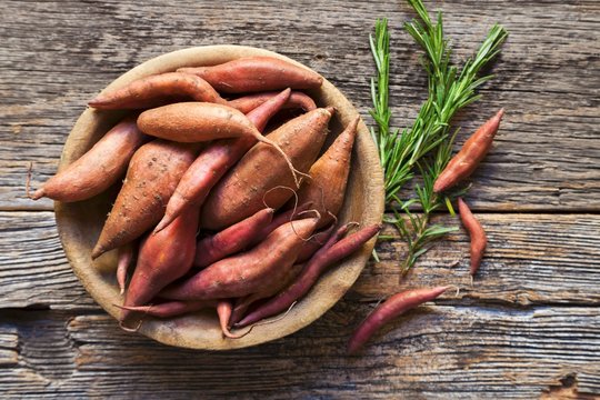 Sweet potatoes in a wooden bowl with sprigs of rosemary