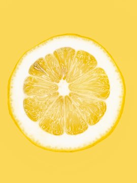 A slice of lemon on a yellow surface, close-up
