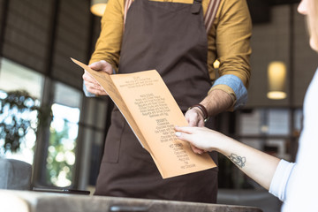 cropped shot of waiter showing menu list to female customer in cafe