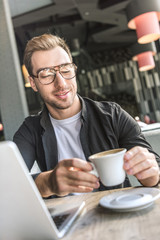 close-up shot of attractive young freelancer with laptop holding cup of coffee in cafe