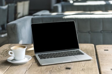 Fototapeta premium cup of coffee and laptop with blank screen on rustic wooden table at cafe