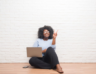 Young african american woman sitting on the floor using laptop at home smiling with happy face...