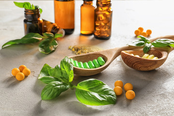 Color pills with fresh basil and bottles of essential oil on grey table