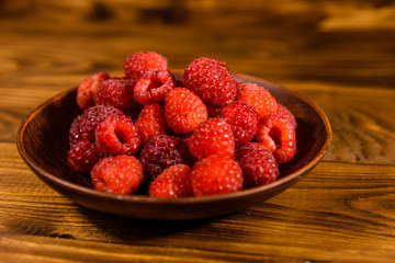 Ceramic plate with ripe raspberries on wooden table