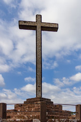 The Cruz Alta viewpoint is the higest point in the Bussaco range in Portugal. The cross monument is under a blue sky with white clouds.