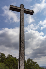 The Cruz Alta viewpoint is the higest point in the Bussaco range in Portugal. The cross monument is under a blue sky with white clouds.