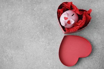 Piggy bank in heart-shaped gift box on grey background. Concept of buying presents for Valentine's...