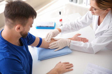 Female doctor preparing patient for blood draw in clinic - obrazy, fototapety, plakaty