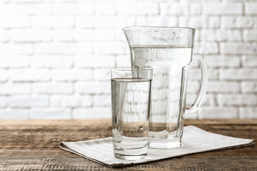 Glass and jug with fresh water on wooden table