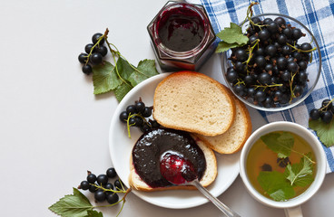 Fresh ripe black currant berries, homemade jam, a cup of currant tea and a loaf of bread with jam...