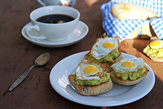 Healthy breakfast, toast with avocado mash and fried quail egg on a brown background.