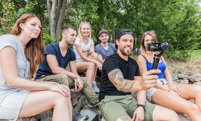 group of six crazy millennials takes a selfie with an action cam based of a handheld gimbal.