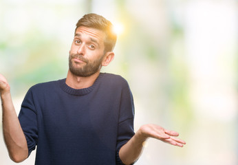 Young handsome man wearing winter sweater over isolated background clueless and confused expression with arms and hands raised. Doubt concept.