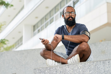 Bearded Indian man in sportswear and glasses resting outdoors and looking into the distance after...