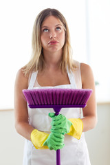 Boring young woman holding broom while cleaning at home.