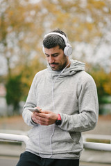 Fit man taking a running workout rest for texting on smartphone and listening music with headphones. Modern sport and running concept.