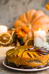Plum cake decorated with sliced plum among the autumn decor - pumpkin, candle, oranges and yellow chrysanthemum. Rustic style. Homely cozy still life