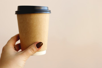 A cup of coffee take away in hand with light pink background