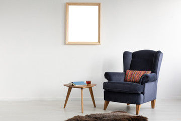 Frame with mockup on white wall of elegant living room with comfortable armchair, coffee table with book and tea and fury rug on white floor