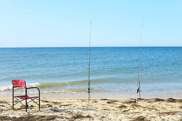 two fishing rods and a chair on the beach. fishing in the early sunny morning with sea background