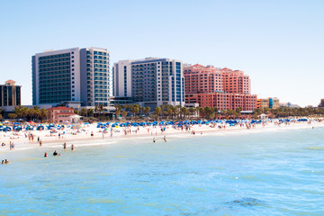 Tropical sandy beach vacation city Clearwater Beach in Florida, colourful beachfront hotel resorts buildings, palm trees, sunbathing tourists, turquoise blue sea waters of Mexican Gulf