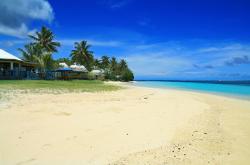 White golden sandy beach and coral blue sea waters with Polynesian beach front houses- traditional fale in Samoa Manase Beach in Pacific Ocean © Radoslav Cajkovic